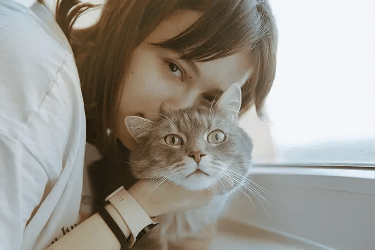 brown-eyed girl holding a green-eyed cat by the head for a photo