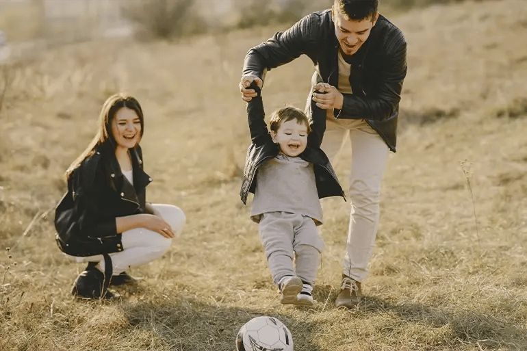 A happy family consisting of a man and a woman playing with their child with the ball.