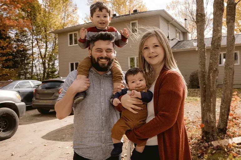 a family with two children, a father and a mother posing for a photo in front of their house