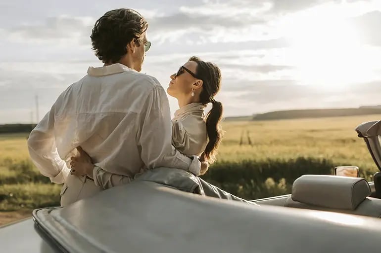 A man and a woman leaning on a car on a cloudy day