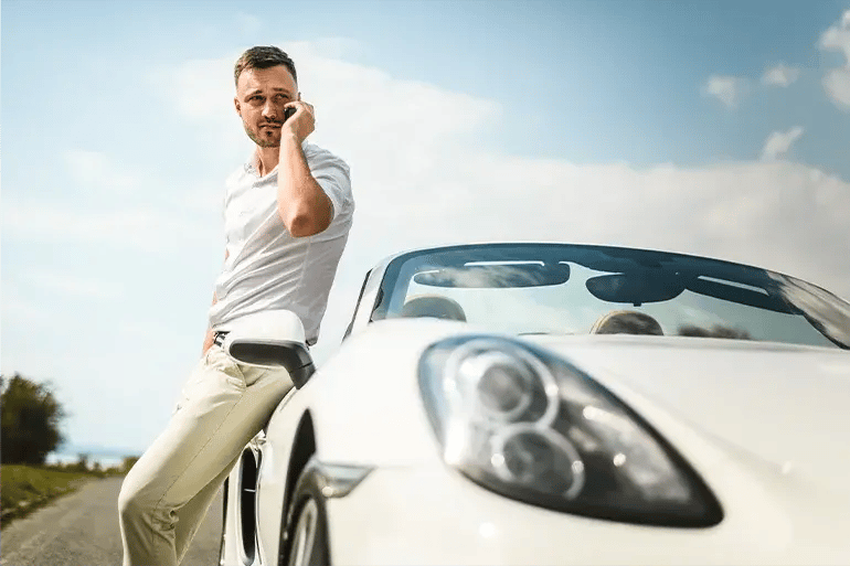 a man talking on the phone leaning on his white sports car
