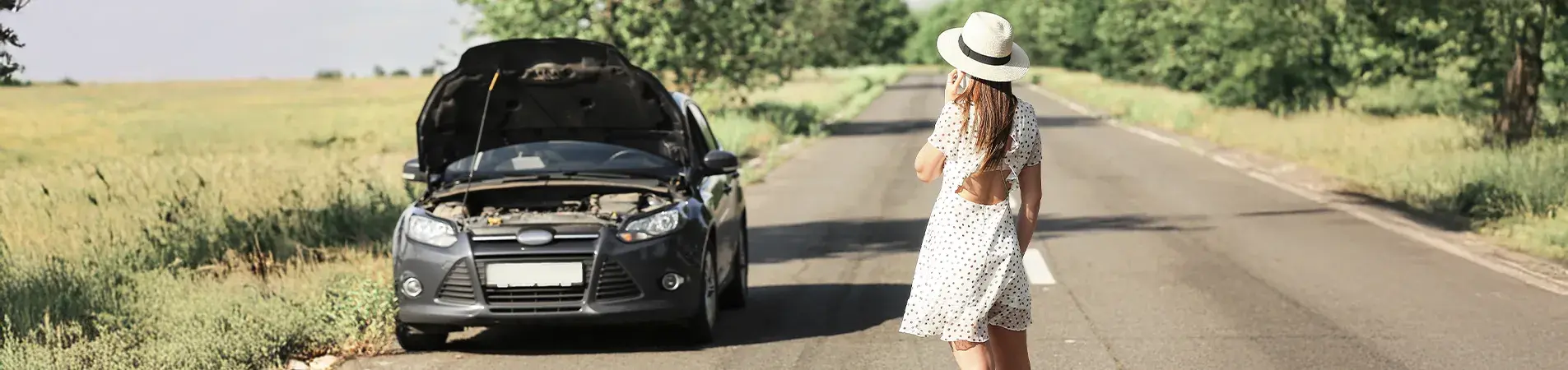woman wearing a hat standing on the road because her car has broken down
