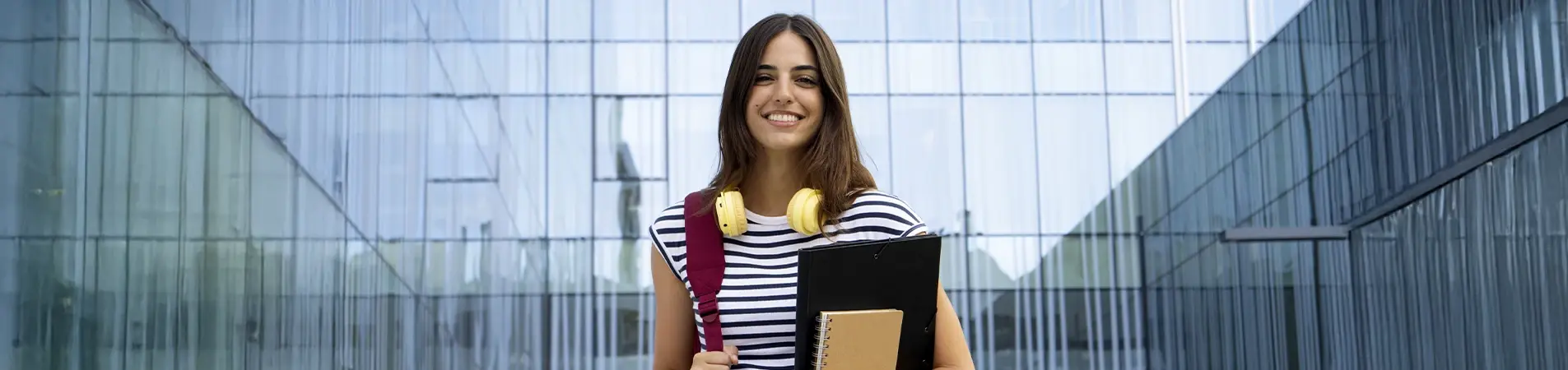 smiling girl with headphones around her neck and holding a folder with books