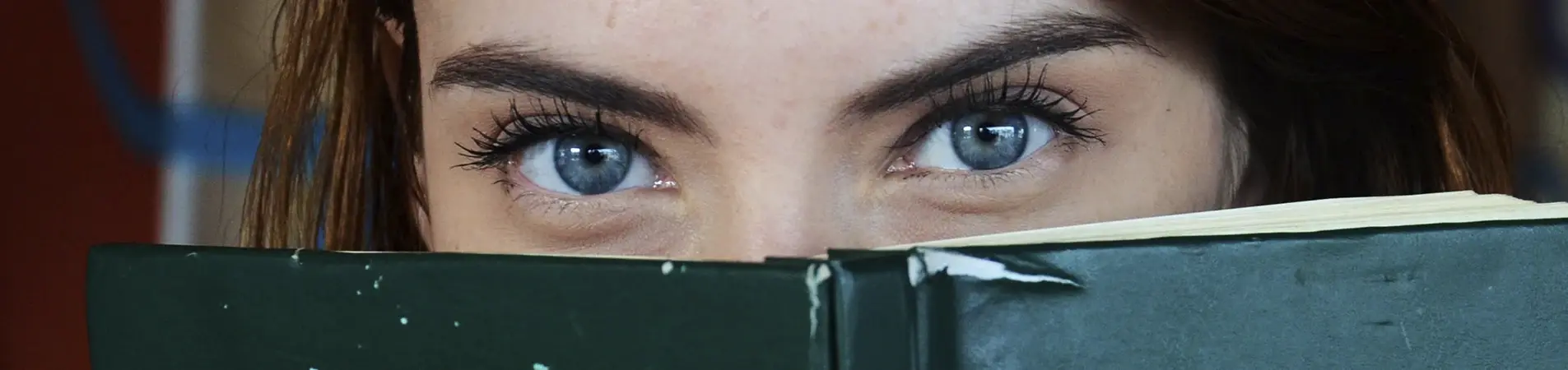 blue-eyed girl peering over a green book