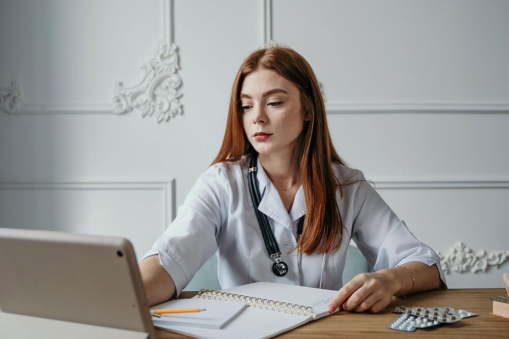 Female doctor working at her desk, looking at a tablet with a notebook and medication on the table. Female doctor working at her desk, looking at a tablet with a notebook and medication on the table.