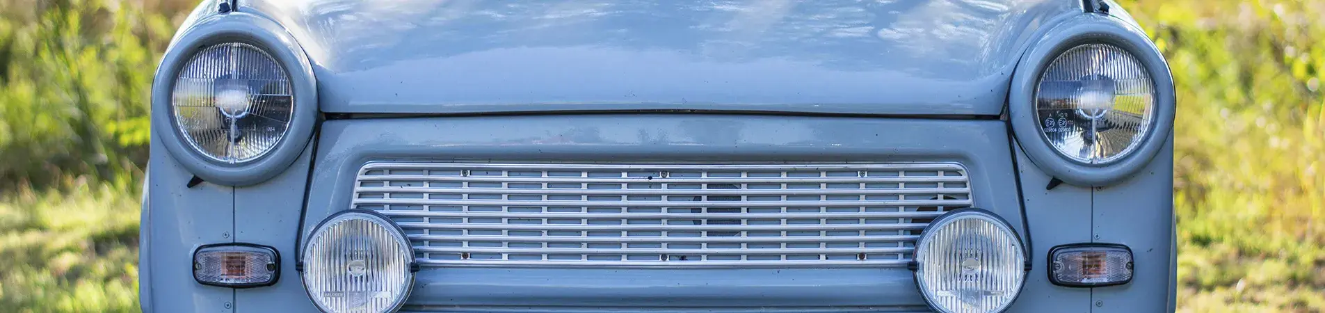 Front view of a light blue classic car parked in a field, representing the potential problems of leaving a car unused, such as exterior wear and tear or mechanical problems due to prolonged inactivity.