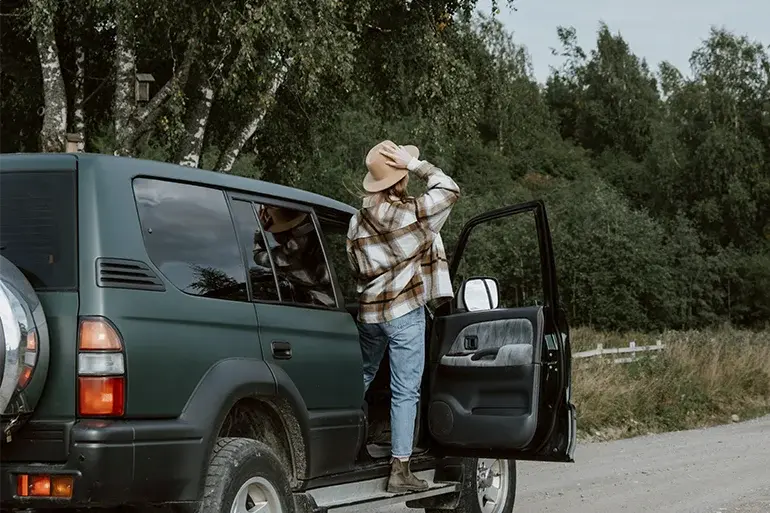 Woman getting out of an SUV stopped on a country road, which may be related to potential problems from leaving a car unused, such as unexpected breakdowns during a trip.